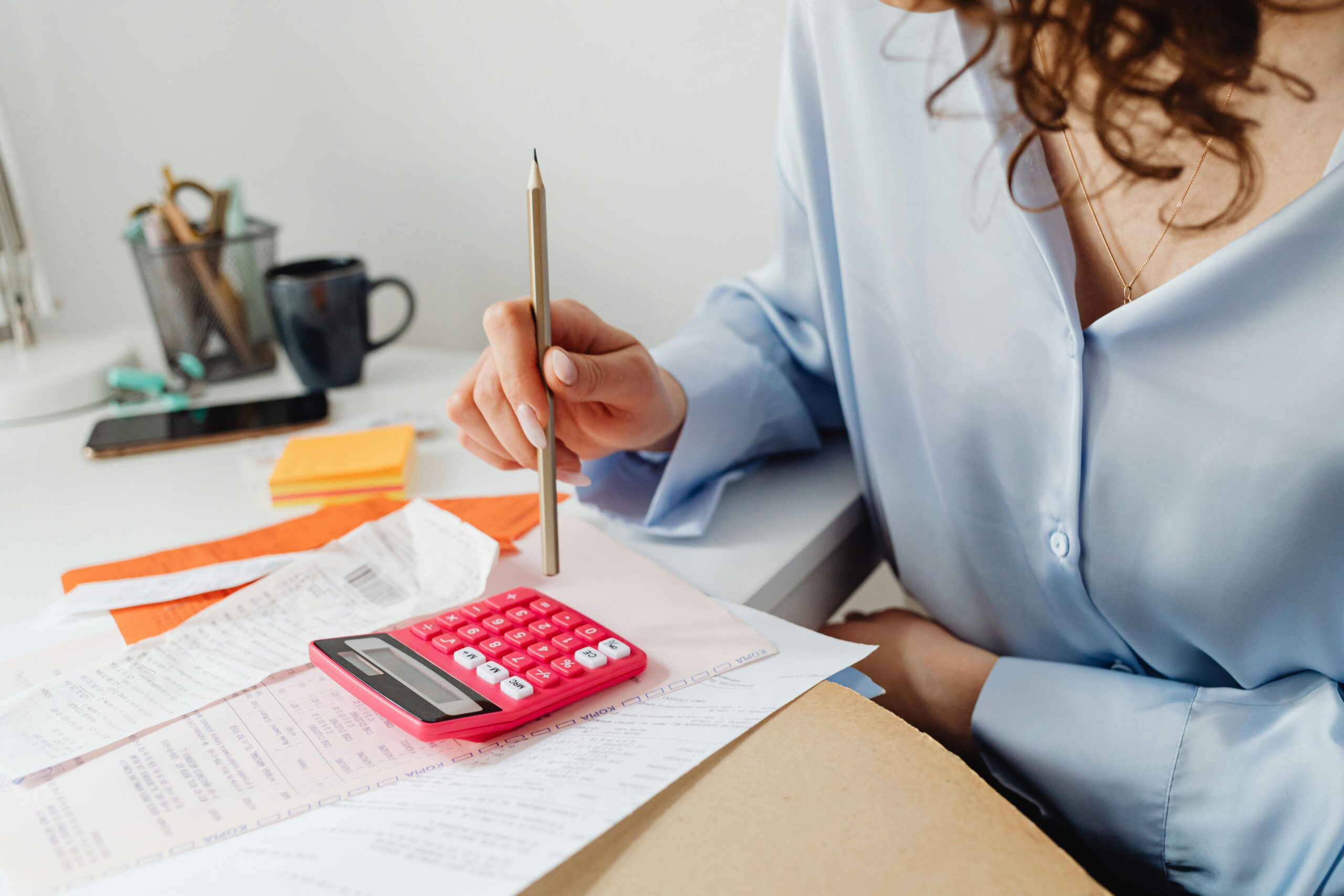 A woman is calculating expenses using a calculator and papers at her desk.